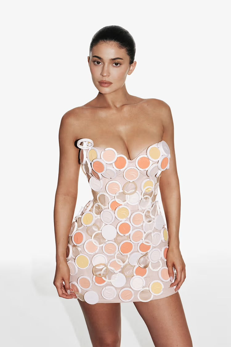 Kylie Jenner in a strapless minidress made from Kylie Cosmetics powder compacts against a white background