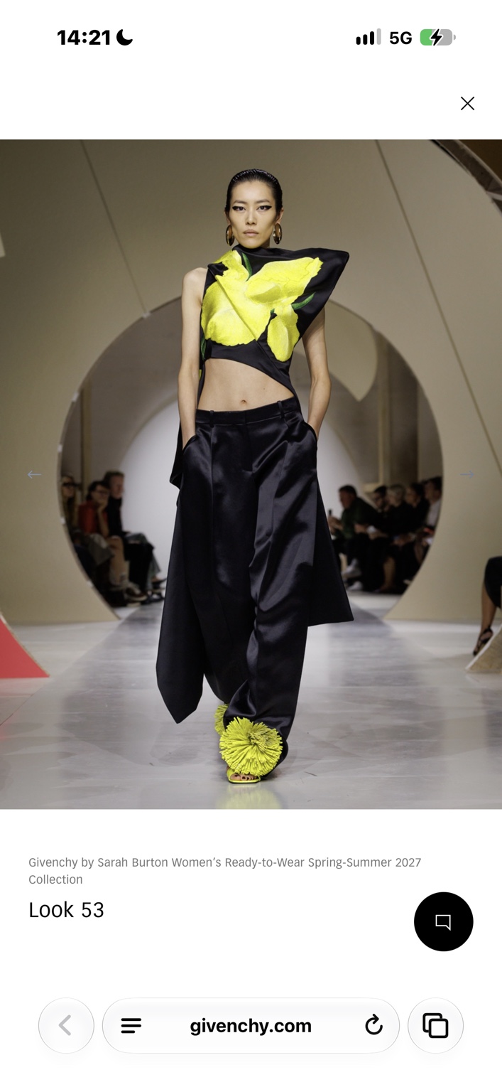 Black satin trousers with a sculptural acid-yellow floral top and pom-pom shoes