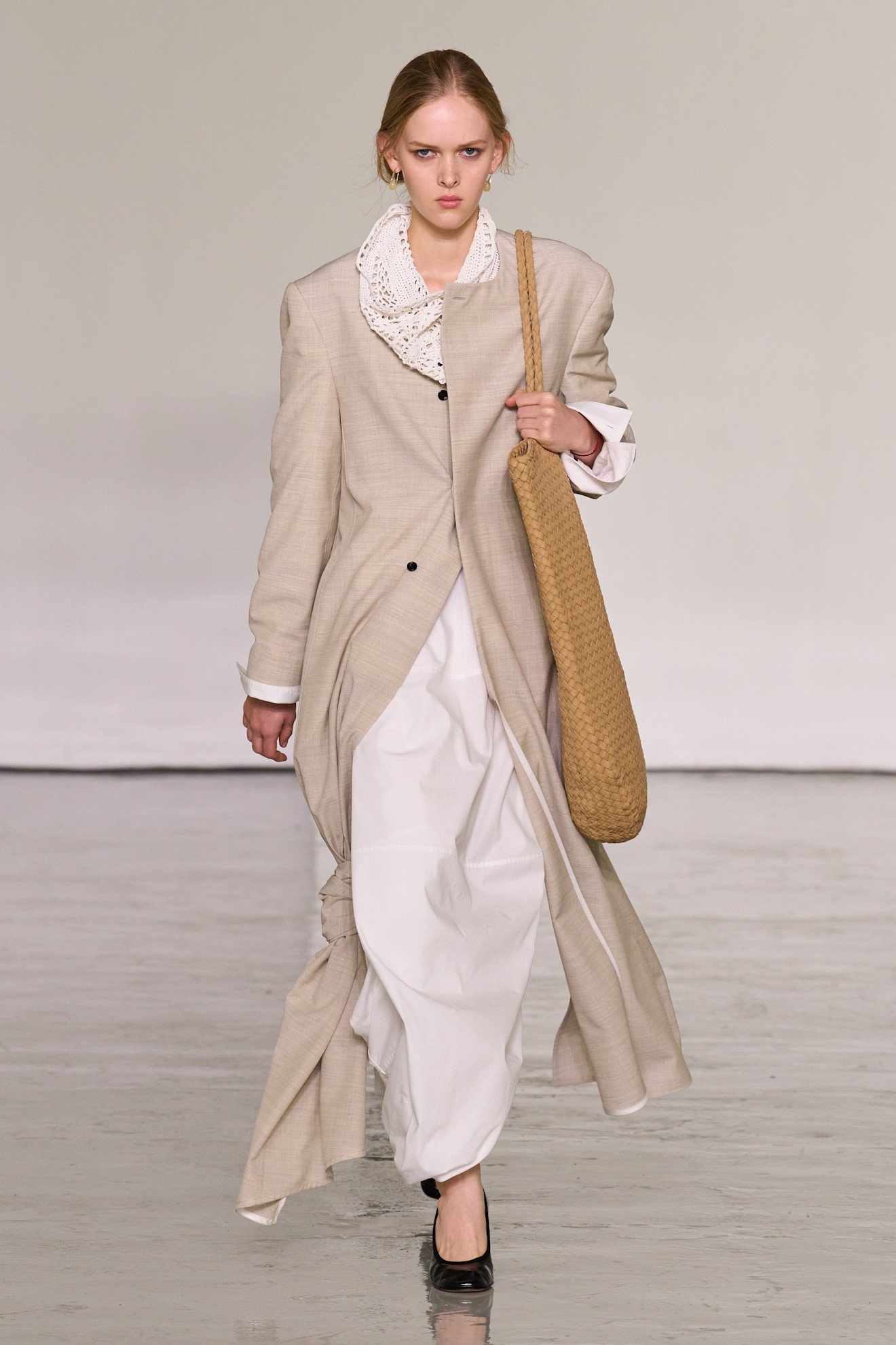 Model in fluid neutral Bottega Veneta layers carrying an oversized woven bag