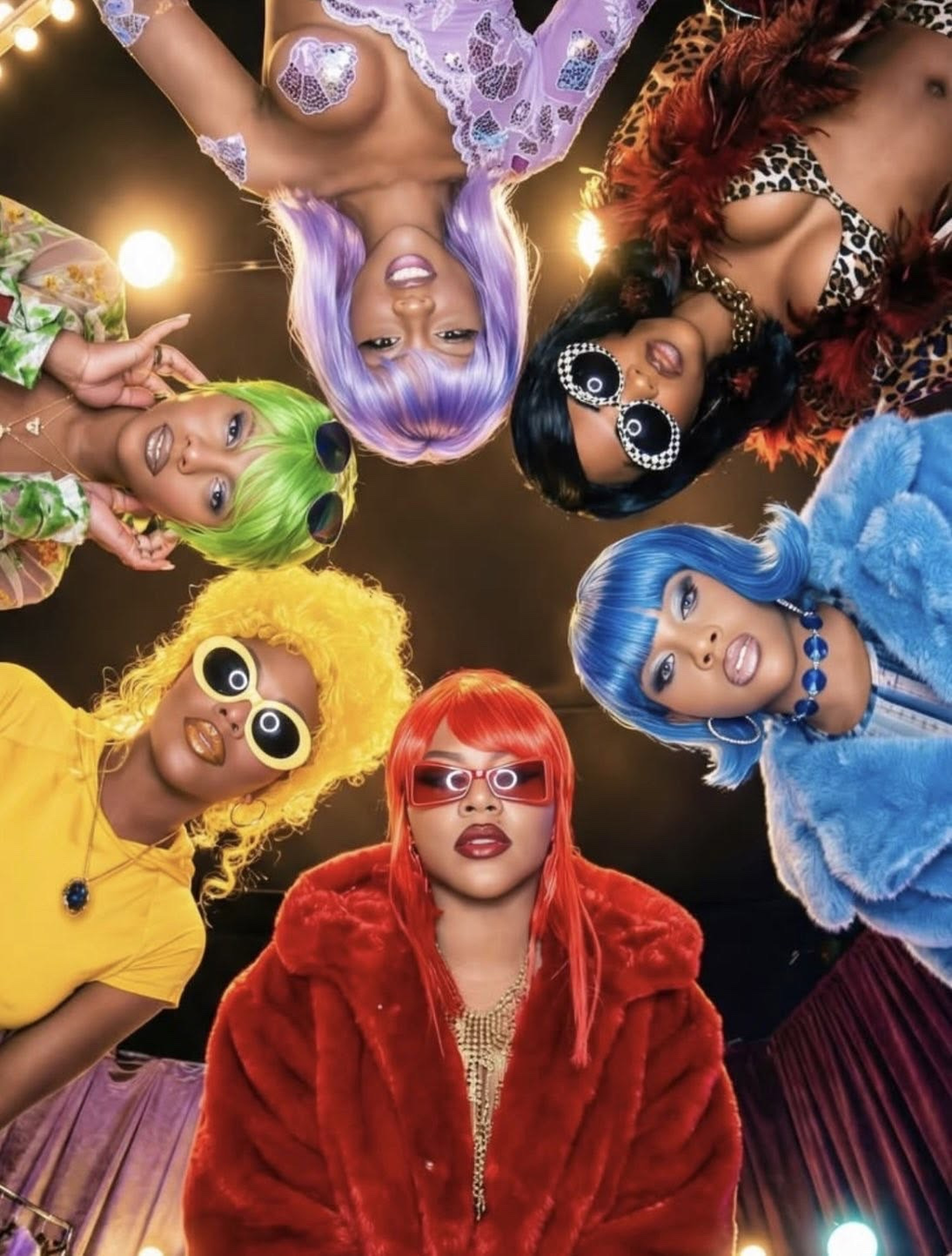 Six women in vivid wigs and colourful fashion looking into the camera