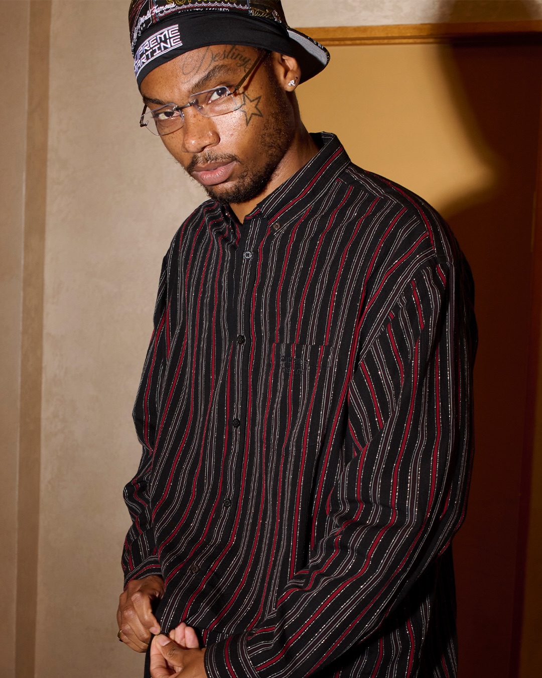 Model wearing a black and red striped shirt and Supreme Martine Rose cap